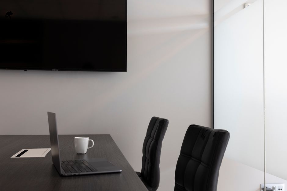 Una configuración de oficina moderna y elegante con laptop, taza y televisor en una sala de conferencias vacía.